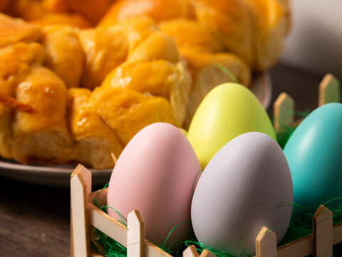 Easter traditional meal on a wooden table. Coloured eggs in basket with bread in the background.