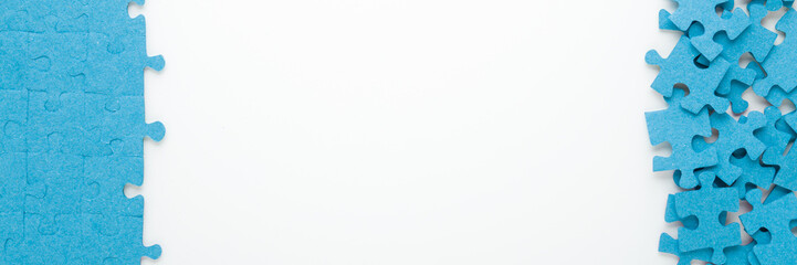 Different many blue puzzle pieces on white table background. Closeup. Jigsaw wide banner. Empty place for text. Top down view.