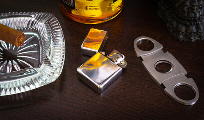 Lighter ashtray cigar cutter and Wisky glass and bottle on wooden table 