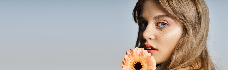 Closeup beauty shot of woman with peach makeup eyeliner, gerbera daisy, face jewels, banner