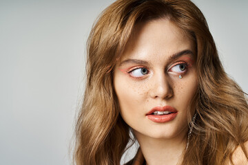 Naklejka premium Closeup portrait of woman with tear face jewels, peach makeup and freckles looking away