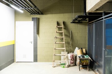 Maintenance area in the basement is pictured, featuring a ladder and several metal cans