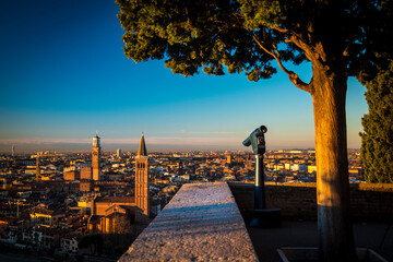 A close up photo of a public monocular on the top of a mountain with spectacular aerial views of the old city of Verona in Italy. Morning gold sunrise