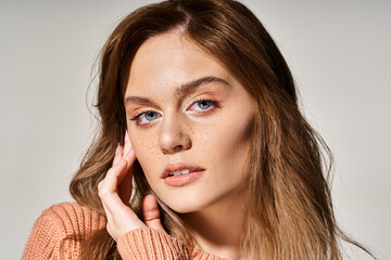 Portrait of pretty woman looking at camera with natural makeup, wearing sweater, touching her face