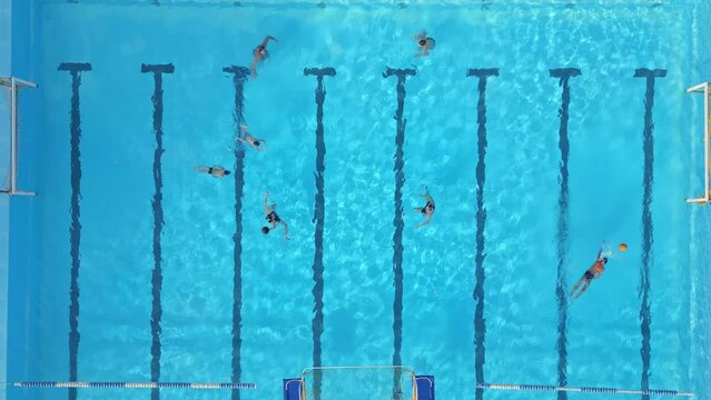 The water polo team players are passing the ball to each other in the water of an outdoor pool as part of their training session before the match