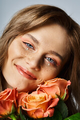 Obraz na płótnie Canvas Closeup photo of smiling woman with peach makeup, face jewels and freckles, holding roses near cheek