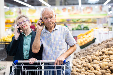 Mature european spouses talking on the phone in supermarket
