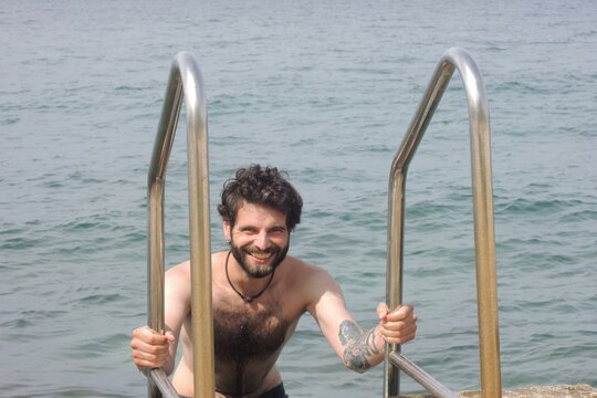 Adventure-seeking man in his 30s, with a rugged beard and tattoos, immersing himself in the refreshing embrace of the sea. This invigorating image captures the freedom and exhilaration of swimming.