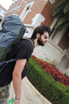 An outdoor adventuristic person with a big backpack passes the town&mdash;a bearded guy, with the sunglasses and tattoos, a rock and roll traveler.