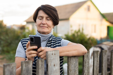 Mature woman standing relaxed near fence talking on phone in backyard smiling