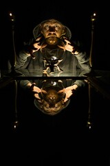 Male fortune teller sitting at a table in front of a crystal ball in a dark room.