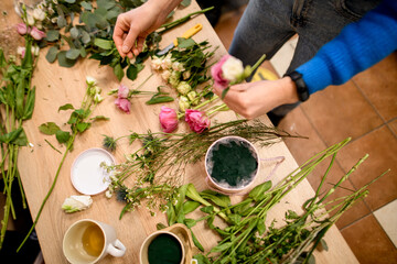 Female hands of the florist hold several sprigs of roses above the table
