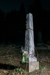 Grave site with a column and a flower at night