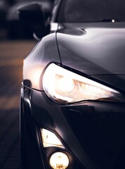 Close-up of a front view of a black car, its headlights and lights on