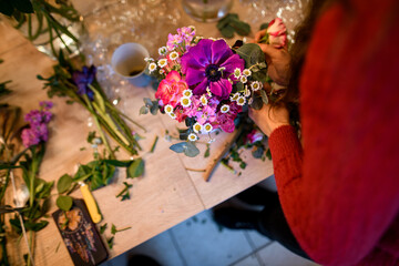 Female hands of a florist are engaged in arranging bouquets of wildflowers above a table