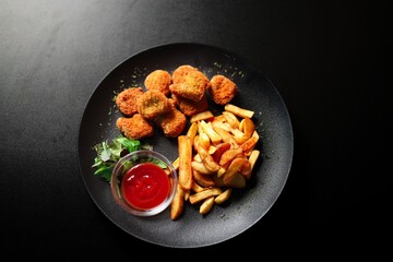 Close-up of a plate of golden-brown chicken nuggets and french fries on a black background