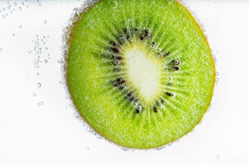 Half of a kiwi fruit floating in a body of water with bubbles in the background.