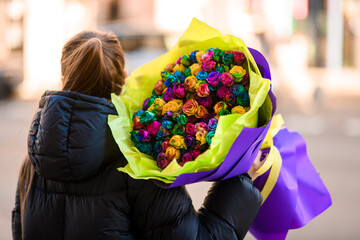 Young woman holding a huge bouquet of multi-colored roses wrapped in wrapping paper on her shoulder