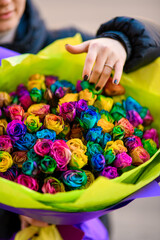 Woman holds a huge bouquet of multi-colored roses wrapped in wrapping paper