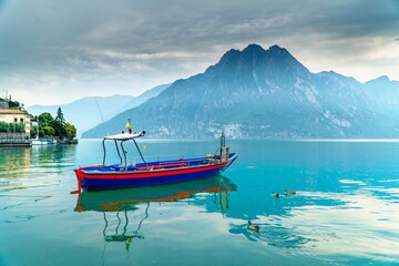 Small blue sailboat suspended in a tranquil Iseo lake in Italy with mountains in the background