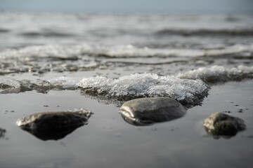 small waves with snow crystals are on the beach next to large rocks