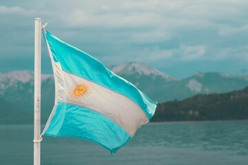 Vibrant Argentinian flag flying in the wind over a tranquil blue body of water - obrazy, fototapety, plakaty