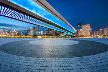 Empty square floor and pedestrian bridge with modern city buildings at night