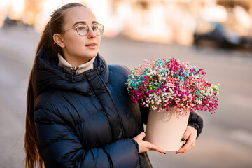 Cute young woman holding a delicate bouquet of multi-colored gypsophila in a gift box