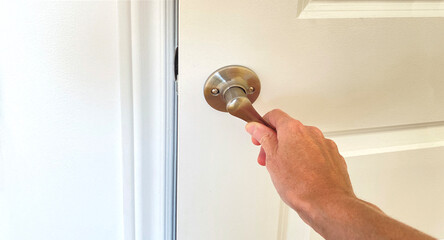 Hand opening a white wooden door. Close-up of a silver metallic door handle opening. Concept of a...