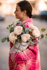 Young smiling girl holding a bouquet of light roses in a vase and looking to the side