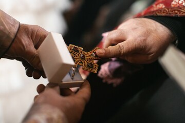 two hands are holding the cross that is placed on a ring
