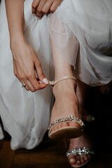 Caucasian bride in a white wedding dress lacing up a pair of white shoes.