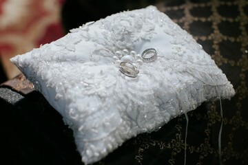 White pillow placed atop a cushion, with two silver rings on either side.