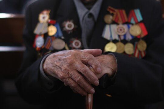 Closeup of the hands of an elderly war veteran with a lot of medals