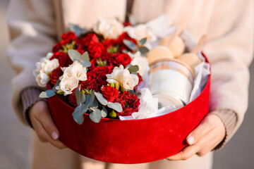Close-up of a red gift box with a composition of roses along with a candle and macaroons
