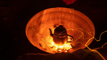 Small metal kettle with hot tea on coals in a fire in Wadi Rum Bedouin Camp at night. Culture and...