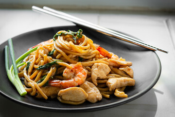 Delicious yakisoba noodles stir-fried with basil and dried chillies. Stir-fried with oyster sauce, soy sauce and chicken fillet, shrimp, decorated with scallions on a black plate. Home cook