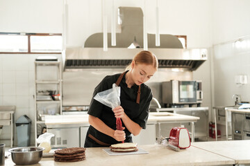 Portrait of a young red haired female pastry chef applying buttercream to a layer of chocolate cake...