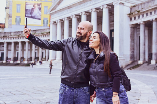 Happy smiling beautiful  Tourists  couple traveling at  Naples Italy, poses and making photos  in front of  Piazza del Plebiscito , Italy.Concept of Italian gastronomy and travel. Italian couple 