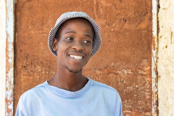single african young man in a village, posing in front of the house brown wall