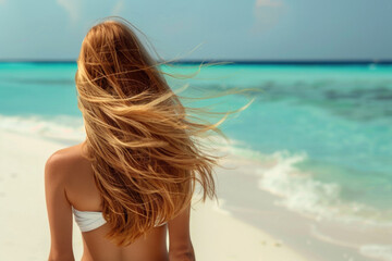 Young woman with long windy hair enjoying the breeze at beach. Beautiful girl relaxing at beach during summer holiday, back view
