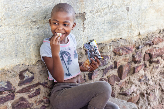 hungry single african girl with shaved head eating some snacks in front of the house in a village,