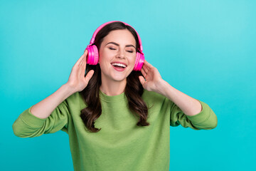 Photo of overjoyed satisfied girl closed eyes hands touch headphones isolated on turquoise color...