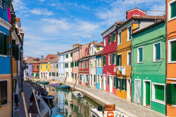 Fototapeta na wymiar Multicolored colorful houses in Venice on the island of Burano. Narrow canal with motor boats along the houses. Summer sunny day. Selective focus.