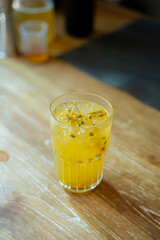 Fresh Look Drink in Yellow Color with Passion Fruit Seeds floating in the glass. Served on the Wooden Table with copy space to input text.