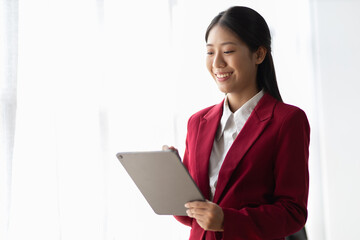 Portrait of attractive Asian businesswoman standing holding tablet in office.