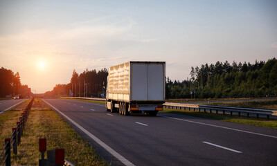 A truck with a tilt semi-trailer carries cargo along the highway in the evening against the...