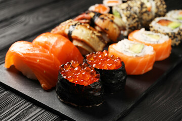 Set of delicious sushi rolls on black wooden table, closeup