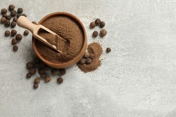 Ground allspice pepper in bowl, grains and scoop on grey table, flat lay. Space for text