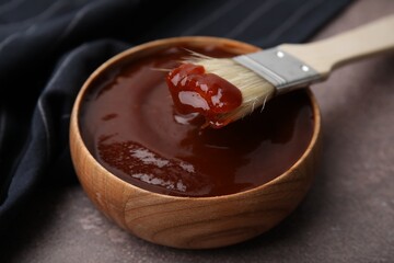Marinade in bowl and basting brush on brown table, closeup